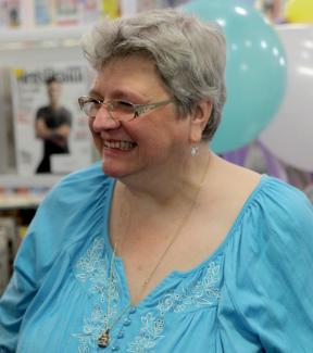 A woman laughing. There are party balloons in the background.